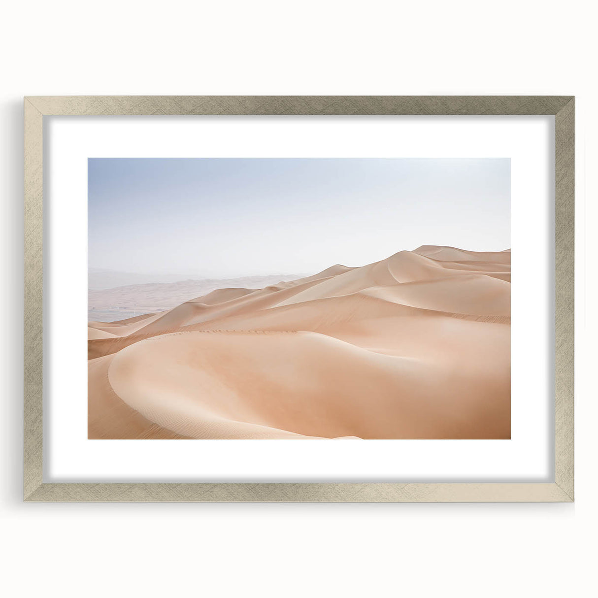 Framed desert landscape wall art featuring warm tones of orange and beige, showcasing a serene sunset over sand dunes, with a sleek silver mat and frame. Perfect for modern home decor.