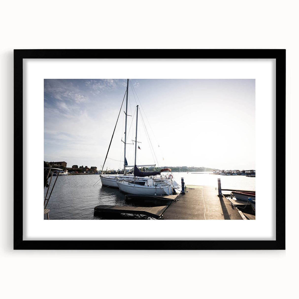 Framed wall art featuring a serene harbor landscape with soft blue and green hues, showcased in a sleek black frame with a mat, perfect for home decor.