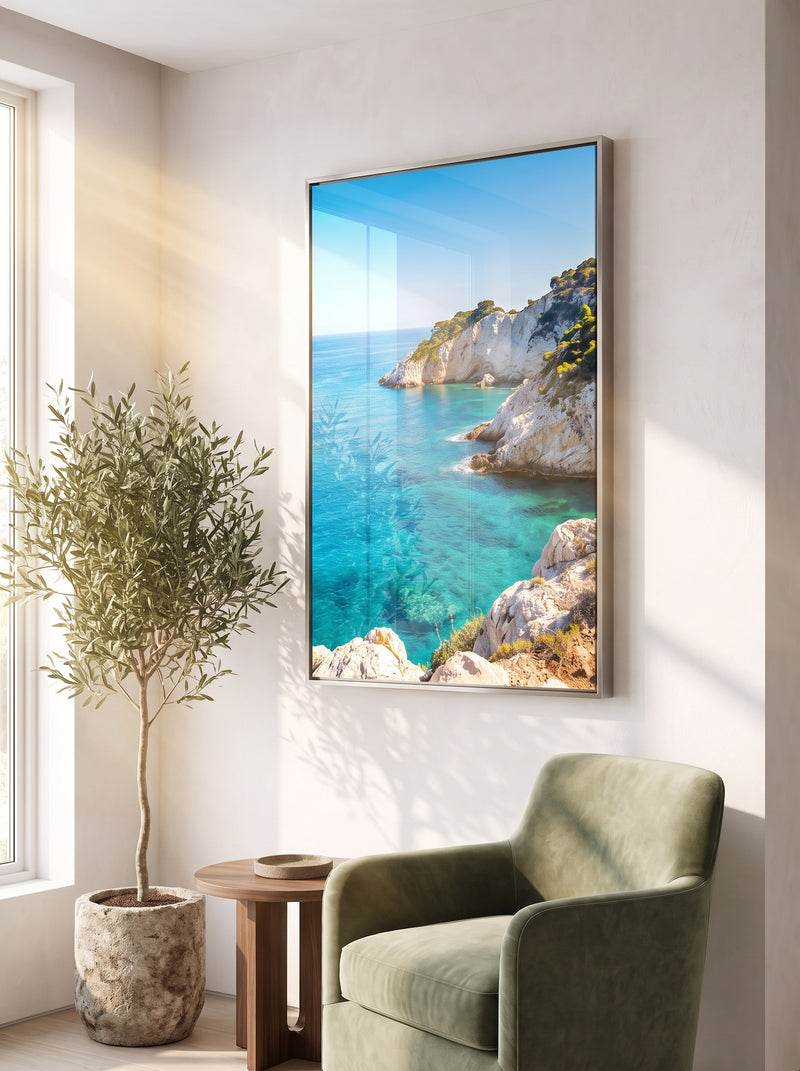 Framed HD metal print of a turquoise sea cove with white cliffs in a slim silver frame beside a green armchair