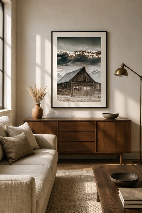 Farmhouse landscape canvas of a rustic barn and mountains in grey and brown, black frame above oak console in sunlit shiplap living room.