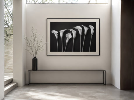 Black-and-white photographic print of white calla lilies, black-framed, above a slim console in a minimalist entryway.