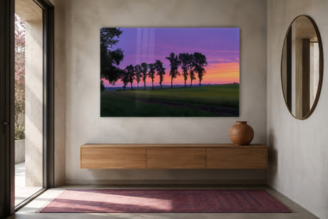 Glass-print landscape of trees at sunset in purple and coral, framed above a floating oak console in a minimalist entryway.
