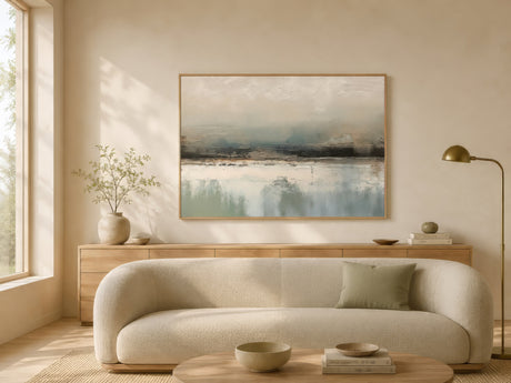 Minimalist abstract landscape canvas in blue, ivory, and brown, framed above an oatmeal sofa in a warm neutral living room.