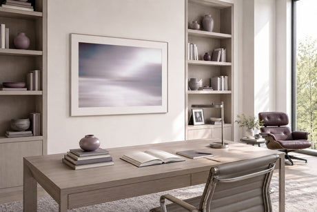 Minimalist long-exposure seascape print in mauve and silver, framed in white above an oak desk in a calm modern home office.