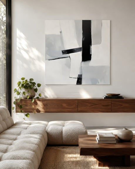 Large black and white abstract painting over floating walnut shelf and cream boucle sofa in sunlit minimalist living room.