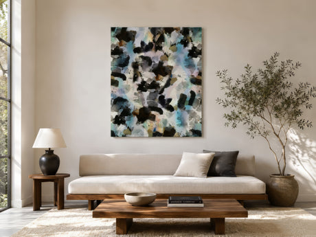 Large abstract painting with black, blue, and cream brushstrokes hung above pale linen sofa in airy neutral living room with olive tree