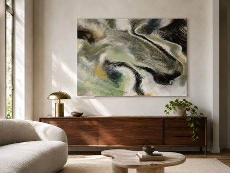 Abstract green and black marbled canvas above wood credenza in sunlit neutral living room with cream chair