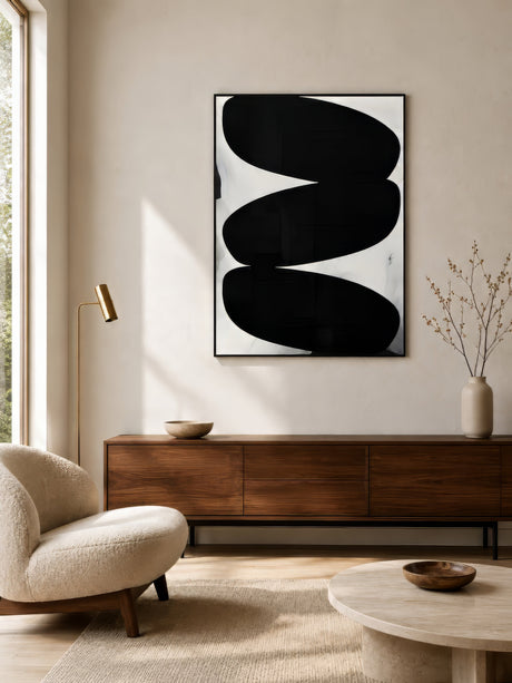 Minimalist black and ivory abstract canvas with curved interlocking shapes, framed and hung in an airy neutral living room with walnut sideboard.