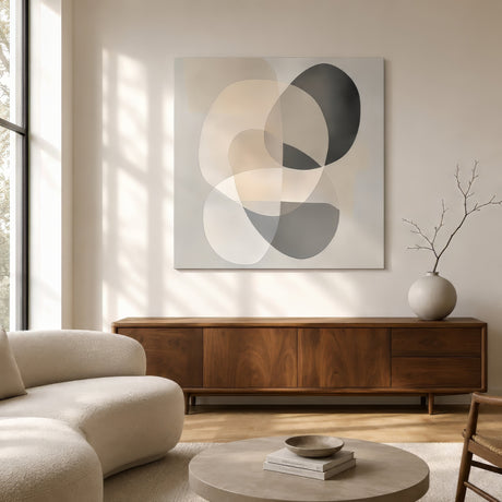 Minimalist abstract canvas of layered circular forms in beige, gray, and charcoal, hung unframed above a walnut sideboard in an airy neutral living room.