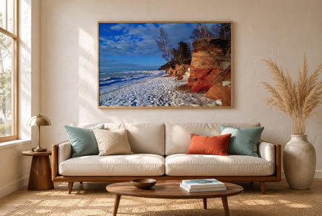 Resort ocean canvas of turquoise sea, red cliffs and white sand in a framed print above a linen sofa, bright airy small apartment living room.