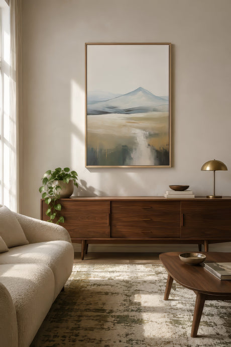 Minimalist mountain valley print in sage and gold, wood frame above a walnut console in a styled neutral living room.