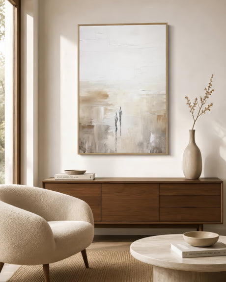 Neutral abstract canvas with two faint figures in cream, ochre, and gray, framed in wood above a walnut sideboard in a sunlit minimalist living room.