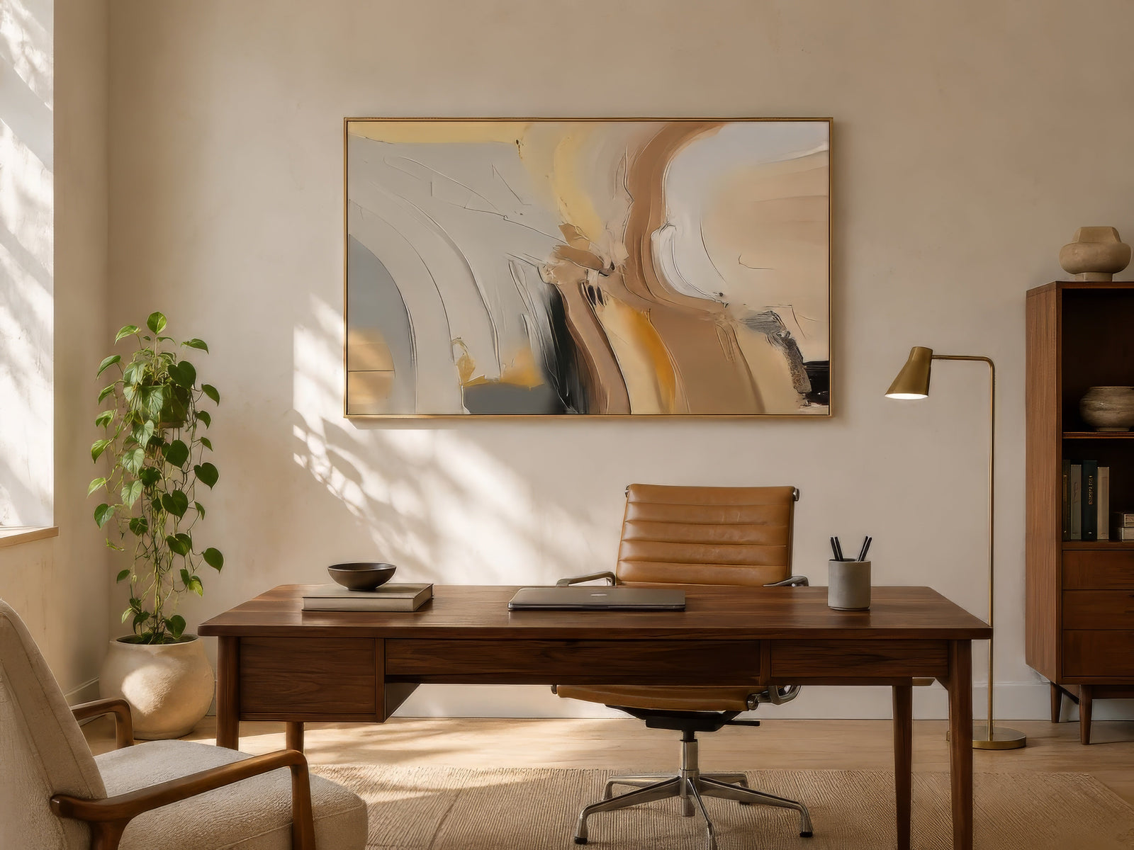 Warm abstract painting with cream, gold, and grey curved strokes in a gold frame above a walnut desk in a sunlit contemporary home office.