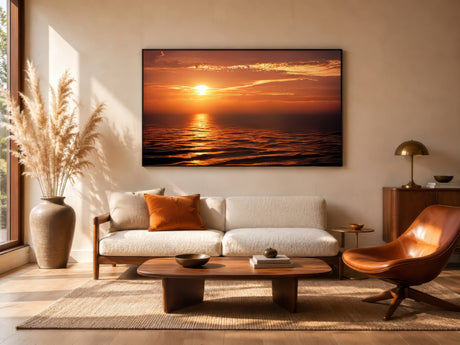 Ocean sunset wall art in amber and orange tones, framed above a linen sofa in a warm modern living room.