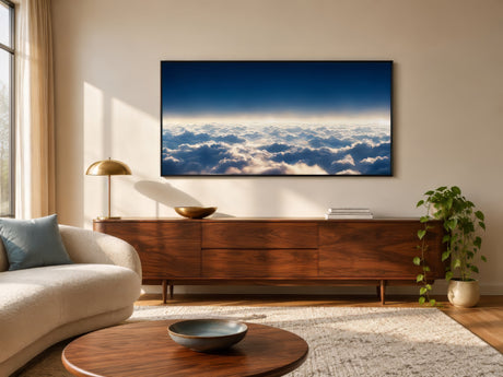 Aerial cloudscape photography print in deep blue and white, framed above a walnut console in a sunlit modern living room.