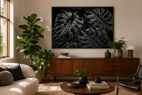 Black-and-green monstera leaf print in dark frame above a mid-century sideboard with fiddle-leaf fig in a cozy living room.