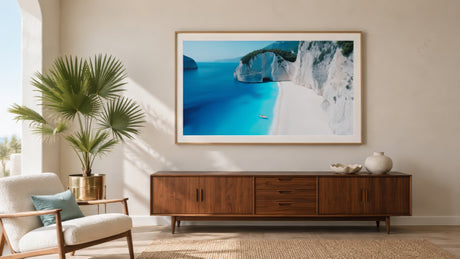 Caribbean coastal canvas of turquoise water and white cliffs in a light wood frame above a teak credenza, spa-style room.