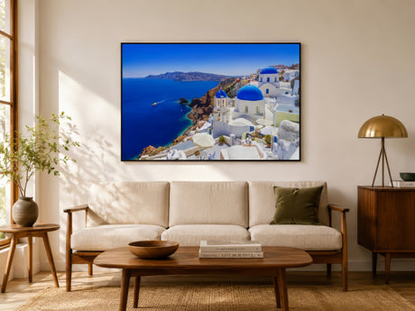 Santorini canvas with blue domes and white architecture above the sea, framed over a linen sofa in a bright coastal living room.