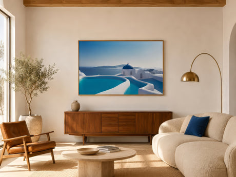 Framed Santorini print with blue domes and turquoise sea, slim oak frame above a wood console in a bright coastal living room.
