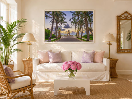 Coastal photography print of a palm-lined Palm Beach drive at sunset, white frame, in a bright living room with rattan chairs and pink peonies.