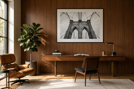 Black and white architectural print of the Brooklyn Bridge arches and cables, framed behind a walnut home office desk for a calm focused mood.