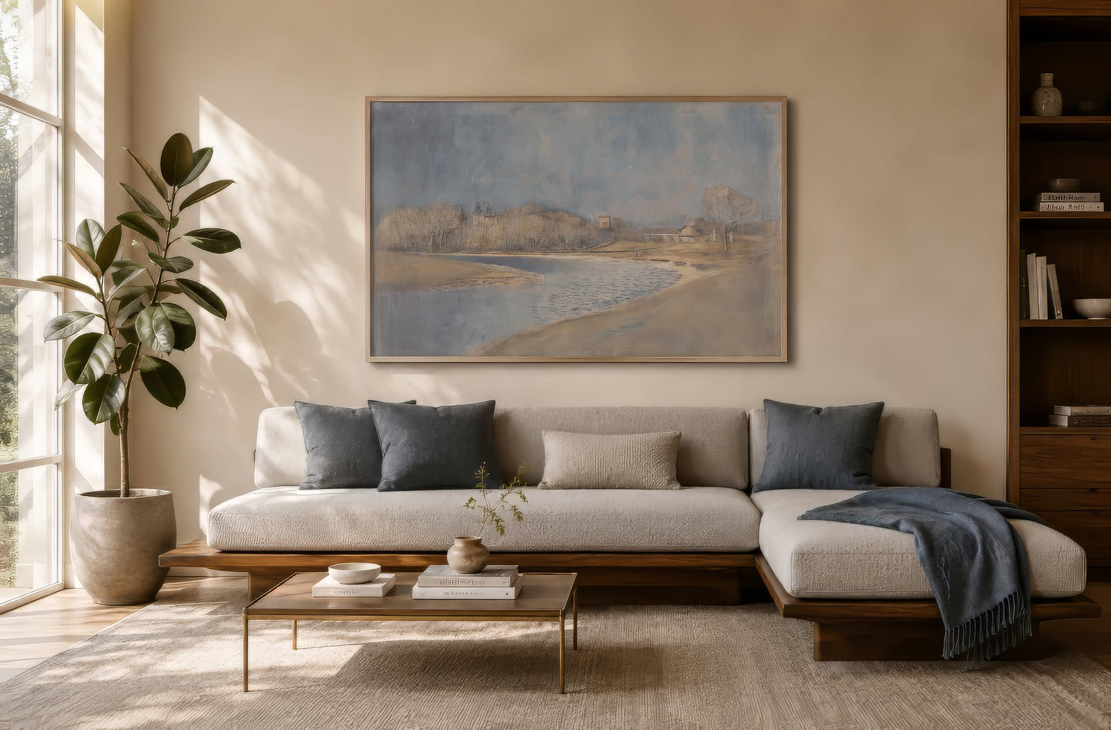 Neoclassical beach and shoreline painting in muted blue and sandy tones, framed above a gray modern sofa in a calm living room.