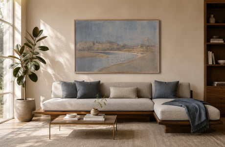 Neoclassical beach and shoreline painting in muted blue and sandy tones, framed above a gray modern sofa in a calm living room.