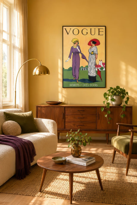 Vintage Vogue poster of two elegant women in purple and white dresses, framed above a sofa in a sunny yellow living room.