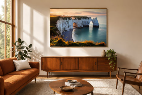 Framed landscape print of Étretat's chalk cliffs and arch in gold and turquoise, hung above a mid-century console in a warm modern living room.