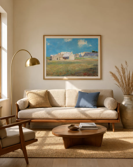 Impressionist Mediterranean village landscape in blue, ochre, and white, framed above a cream sofa in a warm neutral living room.