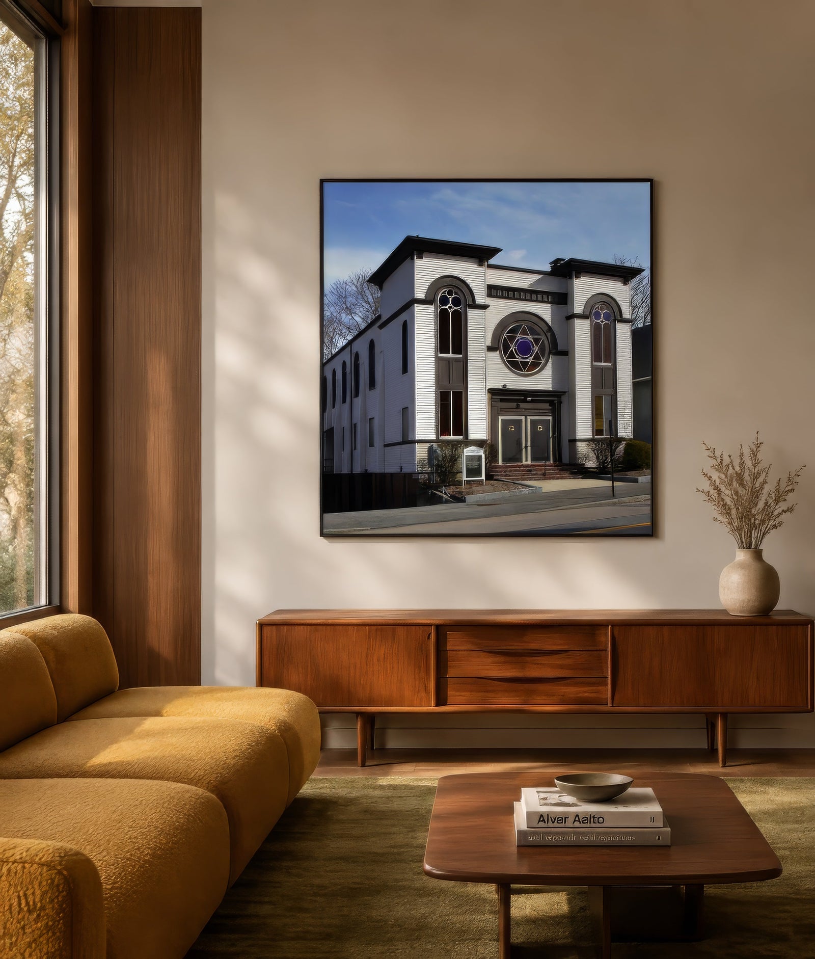 Architectural photographic print of a white-stone synagogue with Star of David window, framed above a wooden console in a warm modern living room.