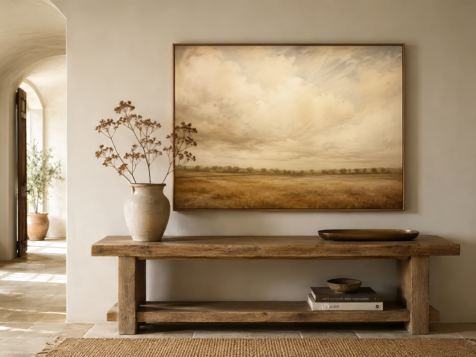 Vintage landscape painting of a golden field and pale sky in a gilt frame above a rustic wood console table in a traditional entryway.