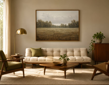 Vintage landscape print of golden meadow and trees in warm oak frame, soft sepia tones, calm neutral living room.