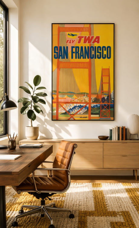 Vintage TWA San Francisco travel poster of the Golden Gate Bridge in red and yellow, framed in black above a wood desk in a sunlit modern home office.