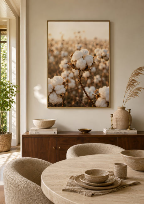 Warm peach photographic canvas of cotton plants in cream and gold, light wood frame, above wood sideboard in cozy dining room.