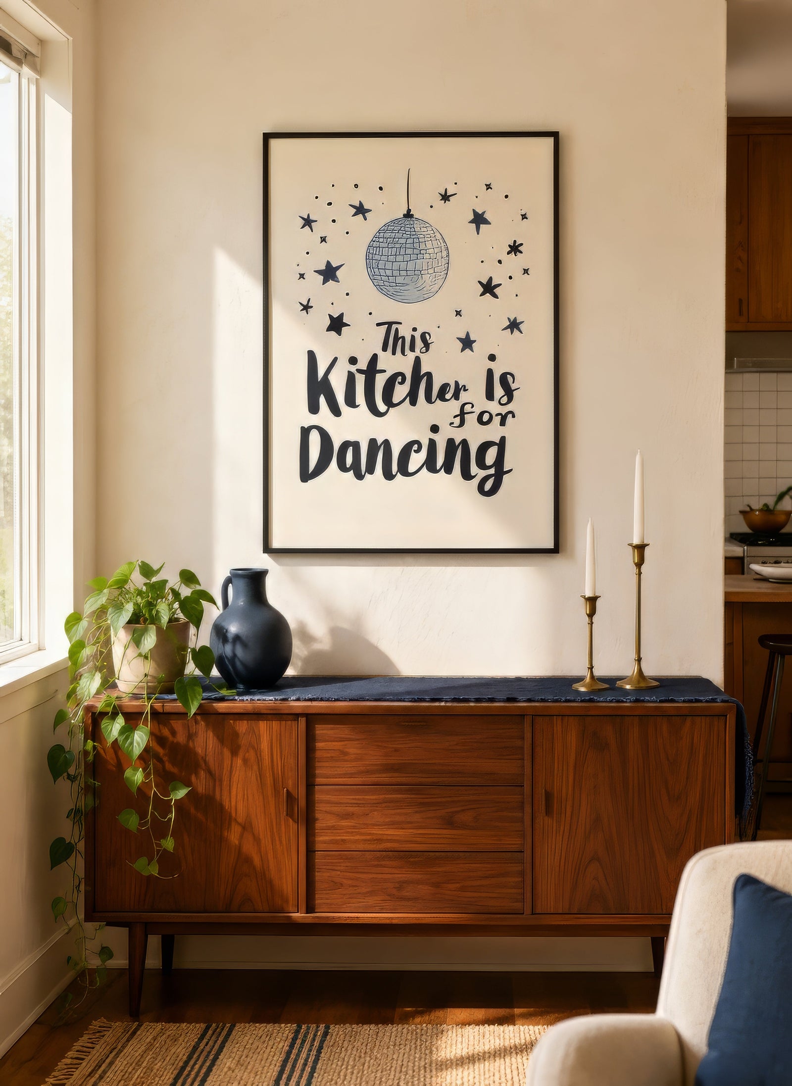 This Kitchen Is For Dancing typography print with navy disco ball and stars, black frame above mid-century credenza in neutral kitchen.