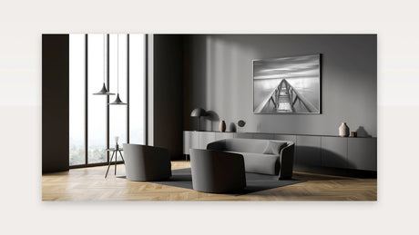Black and white fine art pier photograph in slim matte frame above grey console in modern monochrome living room.