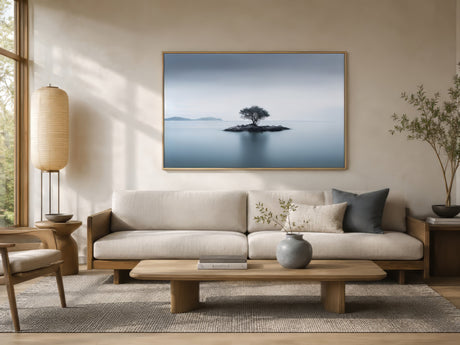 Minimalist abstract canvas of a solitary tree on a rocky island in calm blue and gray tones, framed above a sofa in a light modern living room.