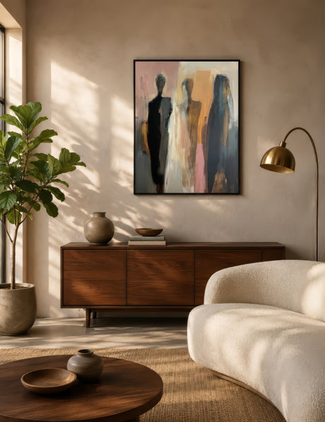 Abstract figurative canvas of three standing figures in pink, ochre, and navy, black-framed above a walnut console in a sunlit modern living room.