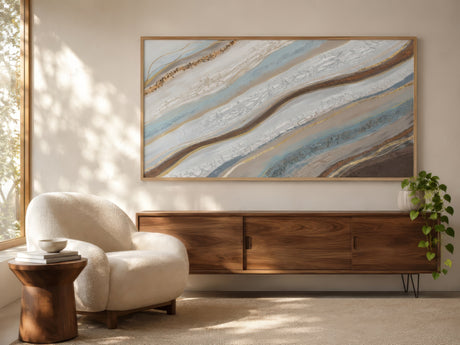Abstract muted blue and beige landscape wall art in wood frame above a linen sofa in a sunlit calm living room.