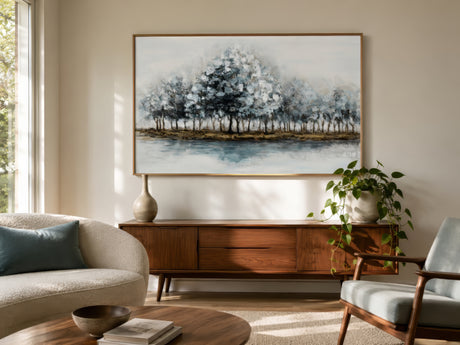 Serene landscape print of soft blue and gold trees over calm water, framed above a sofa in a neutral living room.