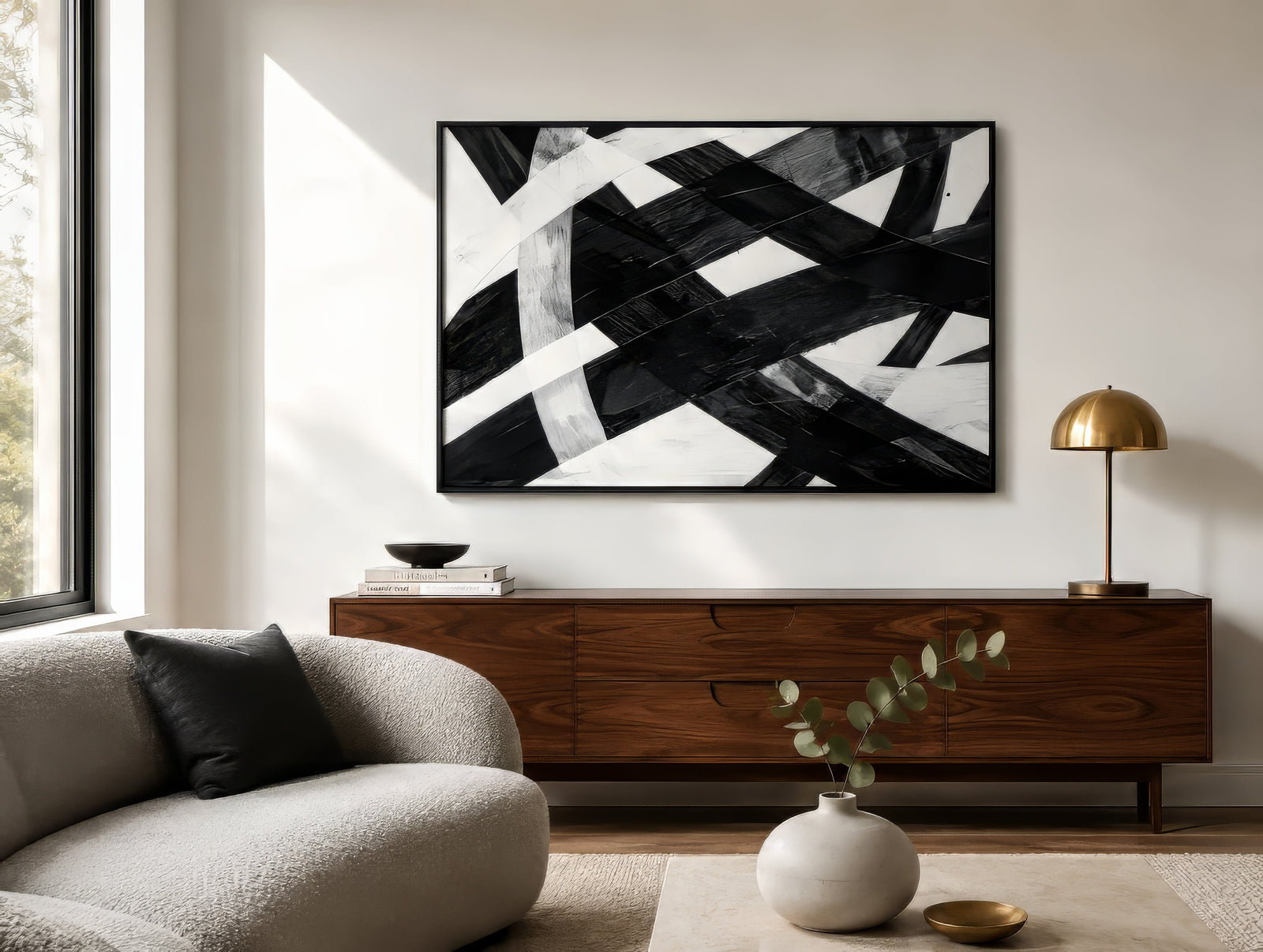 Black and white abstract geometric canvas with crisscrossing brushstrokes, framed above wood sideboard in a calm modern living room.