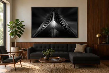 Black and white architectural photography of an angular peaked structure with strong geometric lines, framed above a sofa in a modern living room.
