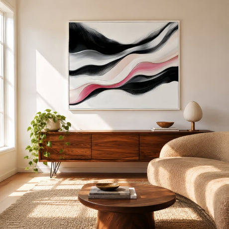 Blush pink and black abstract wave canvas in white frame above walnut credenza in a sunlit neutral living room.