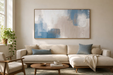Abstract muted blue and gray landscape canvas in a wood frame above a beige sofa, calm nature-inspired living room.