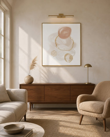 Blush and gold abstract circle artwork in slim gold frame above walnut credenza in warm neutral living room.