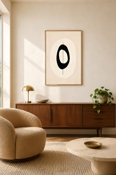 Minimalist abstract canvas with black oval shape on cream, framed in oak above credenza in calm modern living room.