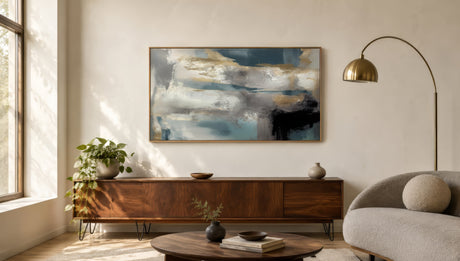 Large horizontal abstract canvas in navy, ochre, and gold framed in wood above a walnut console in a sunlit modern living room.