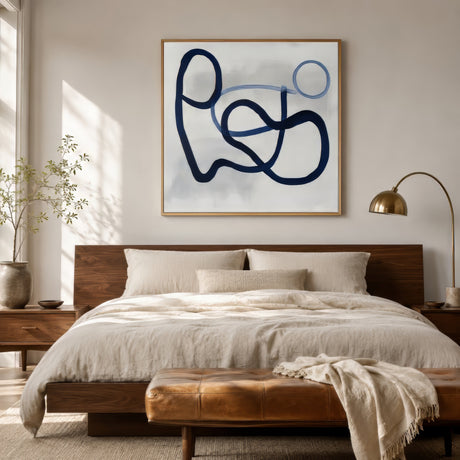 Minimal two-tone navy and blue line art canvas in an oak frame above an upholstered headboard in a calm neutral bedroom.