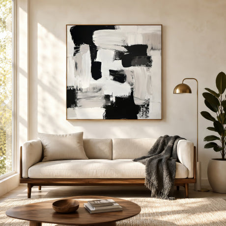 Black and white textured abstract canvas with thick brushstrokes in light oak frame above an ivory sofa in a minimal sunlit living room.